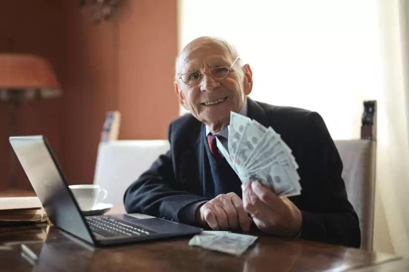 Feliz Empresario Senior Sosteniendo Dinero En La Mano Mientras Trabaja En La Computadora Portátil En La Mesa