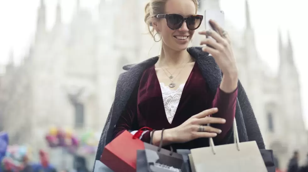 Mujer En Top De Manga Larga Granate Sosteniendo Smartphone Con Bolsas De Compras