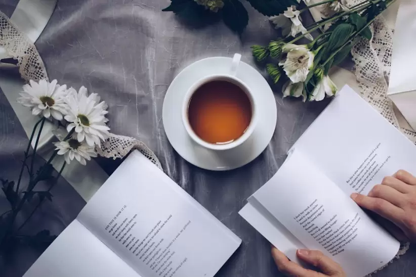 Taza De T De Cermica Blanca Con Platillo Cerca De Dos Libros Sobre Textil Floral Gris