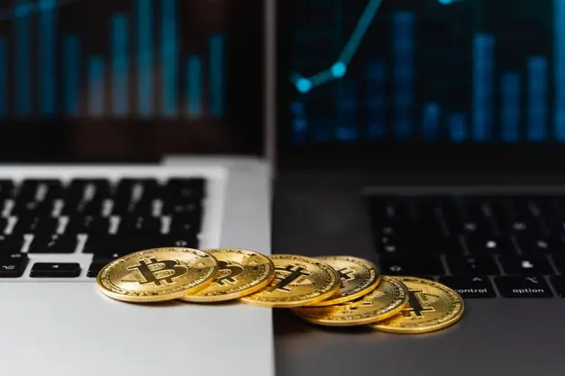 Bitcoins dorados colocados en teclados de portátiles con gráficos financieros digitales de fondo. (Foto: Pexels)