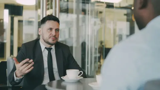 Dos empresarios teniendo una discusión profesional acompañada de café en un ambiente de café moderno. (Foto: Pexels)