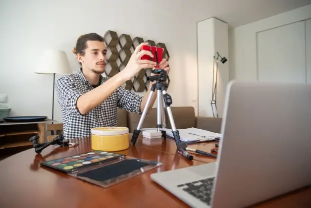 Un vlogger masculino ajusta su cámara en un trípode, preparándose para una grabación en un elegante estudio en casa. (Foto: Pexels)