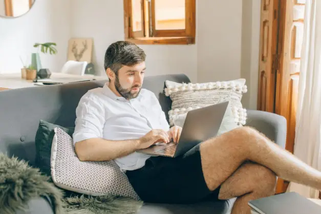 Hombre adulto sentado en el sofá usando un portátil, trabajando de forma remota desde un ambiente acogedor. (Foto: Pexels)