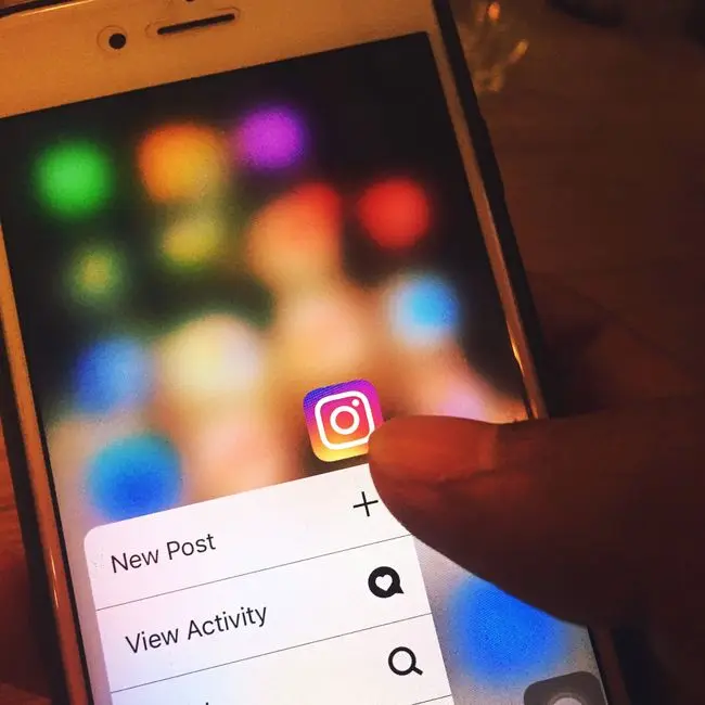 Dedo navegando en la aplicación Instagram en la pantalla de un smartphone con fondo desenfocado colorido. (Foto: Pexels)