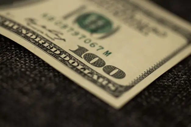 Primer plano detallado de un billete de cien dólares sobre una superficie de tela oscura, mostrando la textura. (Foto: Pexels)