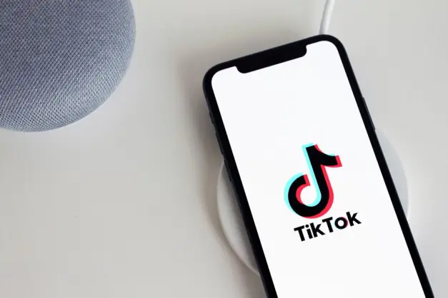 Smartphone que muestra el logo de la aplicación TikTok, colocado sobre un cargador inalámbrico junto a un altavoz inteligente. (Foto: Pexels)