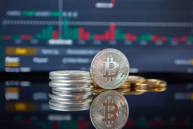 Pila de monedas de Bitcoin frente a un gráfico del mercado de valores, reflejando las tendencias de criptomonedas. (Foto: Pexels)