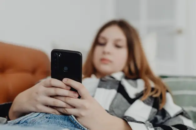 Chica adolescente usando smartphone mientras se relaja en un sofá, representando ocio y conectividad. (Foto: Pexels)
