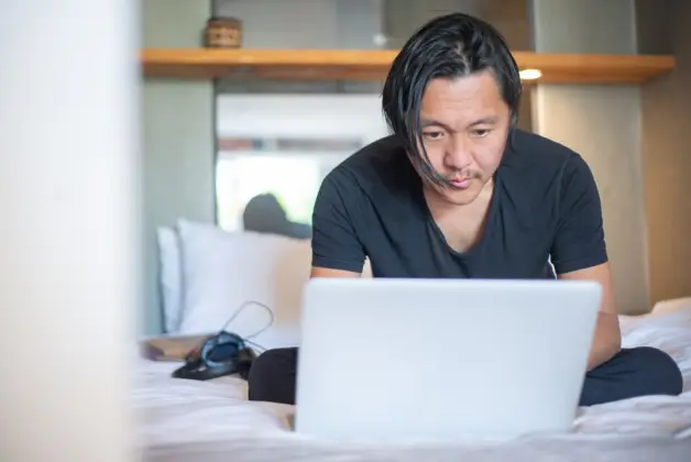 Un hombre asiático trabajando desde casa en un portátil, enfocándose en sus tareas digitales en un ambiente acogedor. (Foto: Pexels)