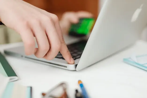 Vista cercana de manos operando un portátil mientras sostienen una tarjeta de crédito, mostrando compras en línea o trabajo. (Foto: Pexels)