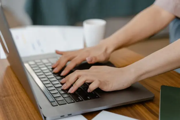 Primer plano de una mujer escribiendo en un portátil en un ambiente interior acogedor, enfocándose en la productividad. (Foto: Pexels)