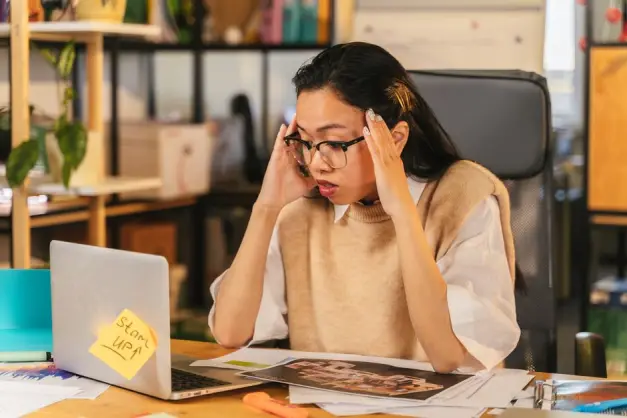 Una mujer con gafas muestra estrés mientras trabaja en un portátil en un entorno de oficina. (Foto: Pexels)