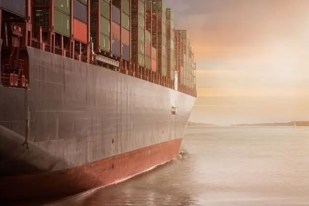 Un colosal buque de carga cargado de contenedores navega a través de aguas tranquilas contra un vibrante cielo al atardecer. (Foto: Pexels)