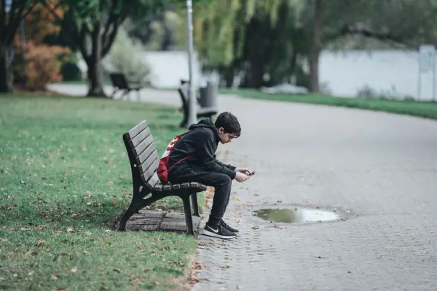 Chico adolescente sentado en un banco del parque usando su smartphone, rodeado de naturaleza. (Foto: Pexels)