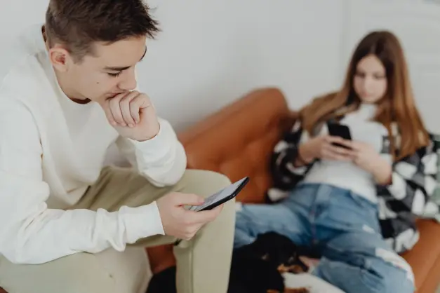 Dos adolescentes sentados casualmente en un sofá, absortos en sus smartphones en interiores. (Foto: Pexels)