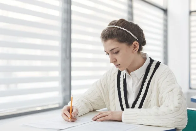 Estudiante concentrada mientras escribe durante un examen en un aula iluminada.