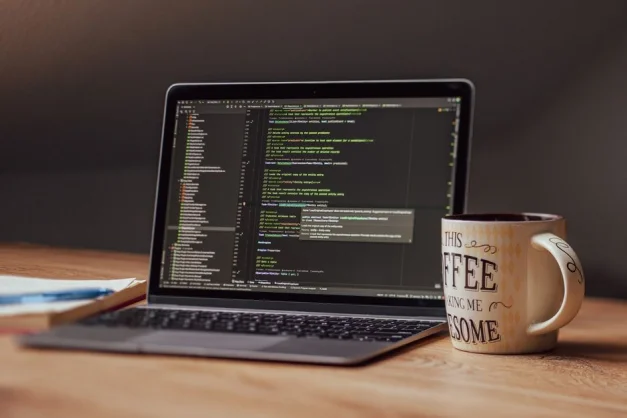 Laptop mostrando un editor de código con una taza de café en el escritorio, perfecto para temas tecnológicos.