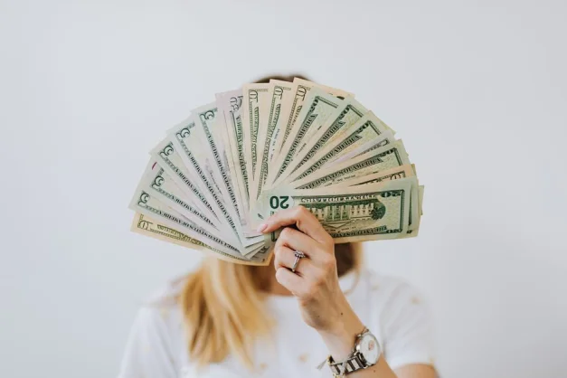Primer plano de una persona sosteniendo un abanico de billetes de dólar sobre un fondo neutral.