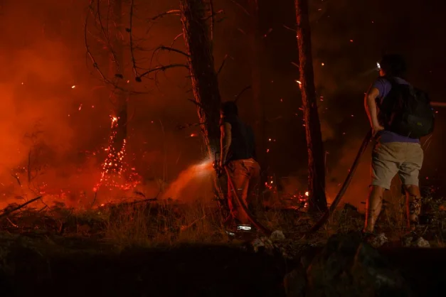 Escena dramática de bomberos combatiendo un incendio forestal bajo cielos oscuros y llenos de humo.