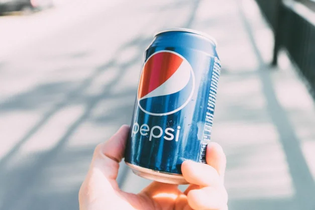 Lata de Pepsi refrescante sostenida en la mano en un día soleado. Perfecta para anuncios.