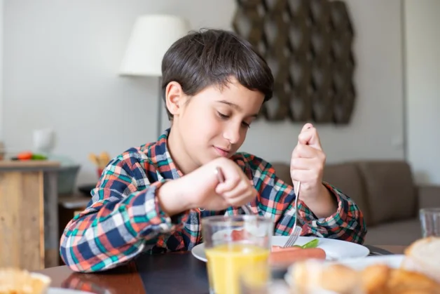 Un niño pequeño desayunando en casa en un ambiente acogedor, mostrando la rutina y la etiqueta diarias.