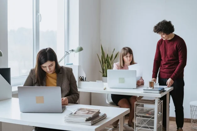 Grupo de colegas trabajando juntos en un espacio de oficina moderno y luminoso con laptops.