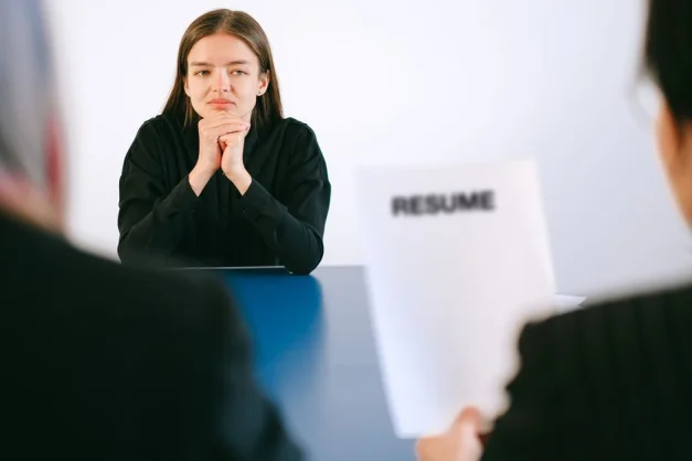 Una mujer en una entrevista de trabajo frente a dos empleadores con enfoque en su currículum.