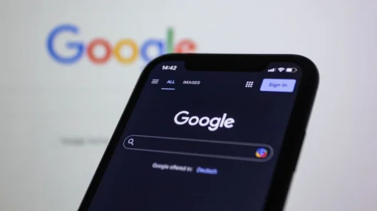 Pantalla de smartphone mostrando la búsqueda de Google en modo oscuro con el logo de Google de fondo.