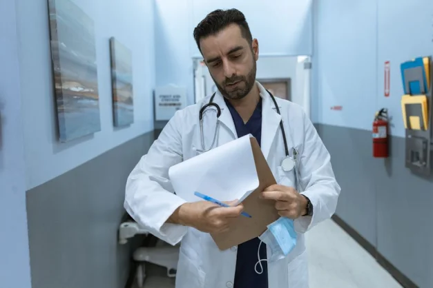 Un médico en bata revisa un historial médico en un pasillo de hospital.