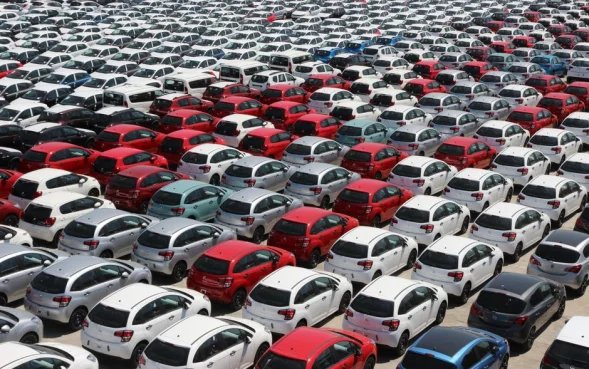 Toma aérea de coches coloridos estacionados ordenadamente en un gran estacionamiento al aire libre bajo la luz del sol.
