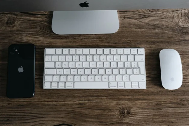 Un espacio de trabajo minimalista con un teléfono inteligente, teclado y ratón sobre un escritorio de madera.