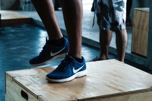 Primer plano de zapatillas Nike azules sobre una caja pliométrica durante el entrenamiento en el gimnasio.