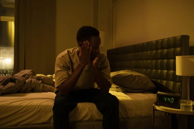 Hombre afroamericano sentado en una cama luchando contra el insomnio por la noche.