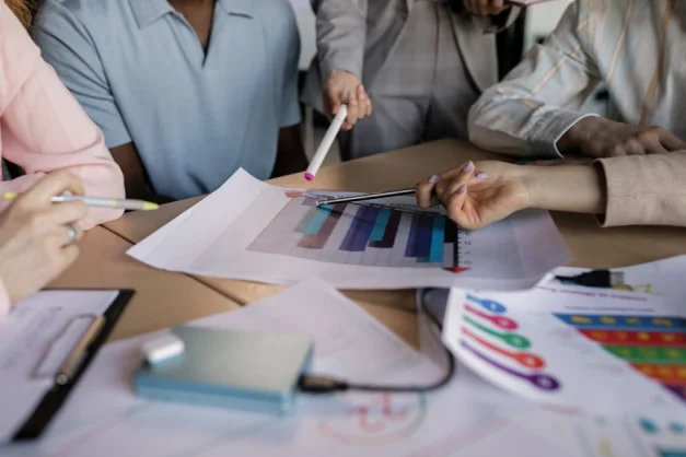 Un equipo diverso involucrado en la planificación y discusión de una estrategia empresarial alrededor de una mesa de madera en interiores.