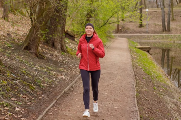 Mujer con chaqueta roja corriendo por un sendero forestal durante la primavera.